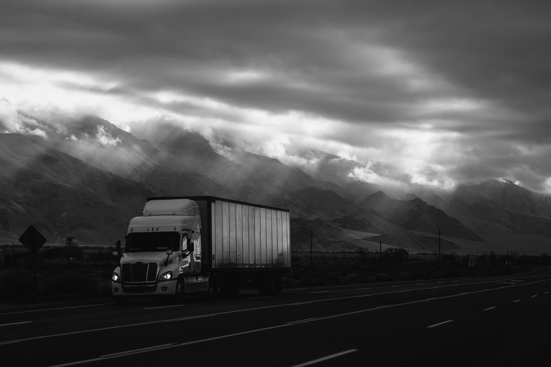 Semi-truck driving down a road at sunset